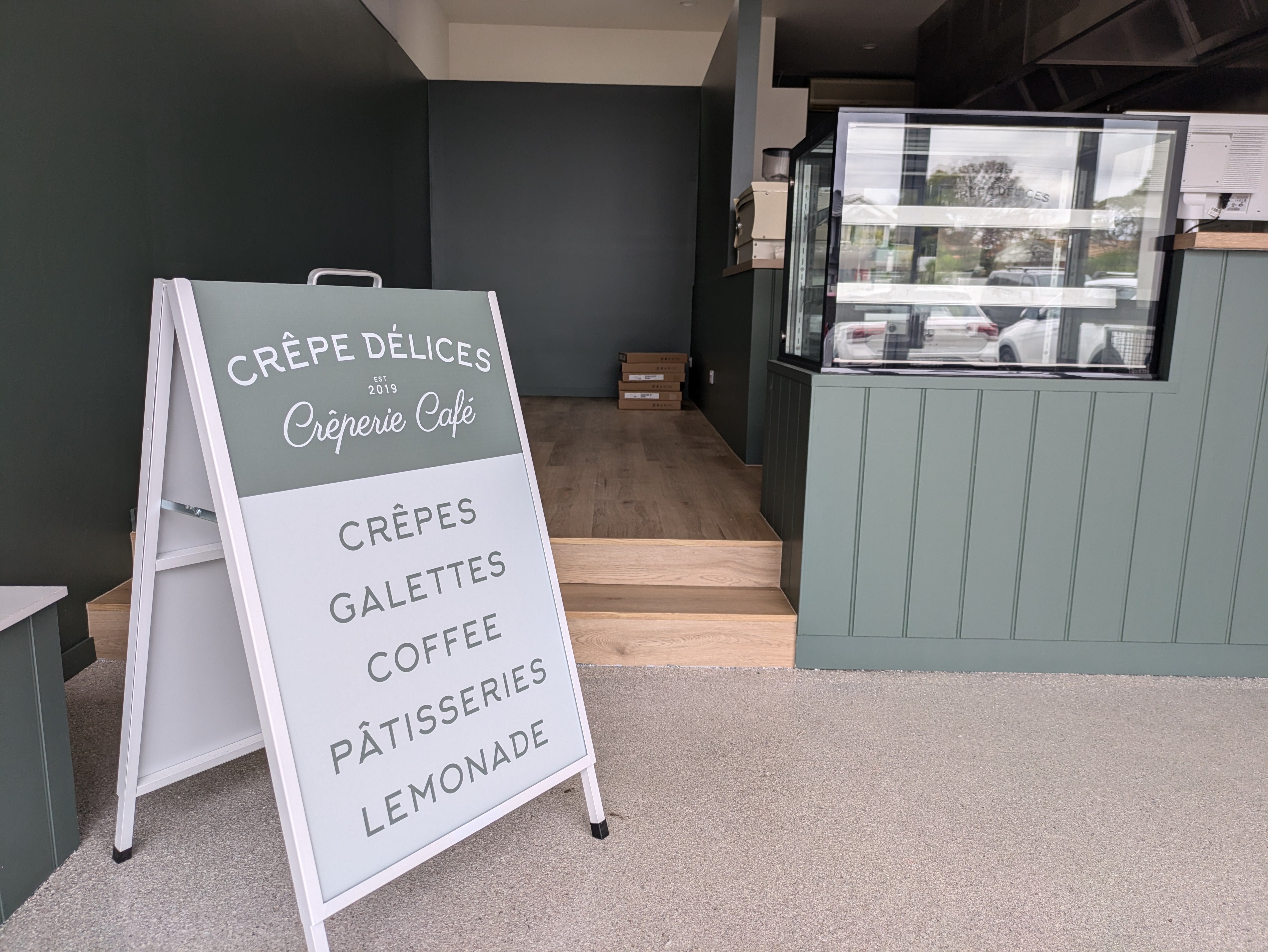 Outdoor sign for Crèpe Délices with a cafe counter in the background by Saltwater Sign Co.