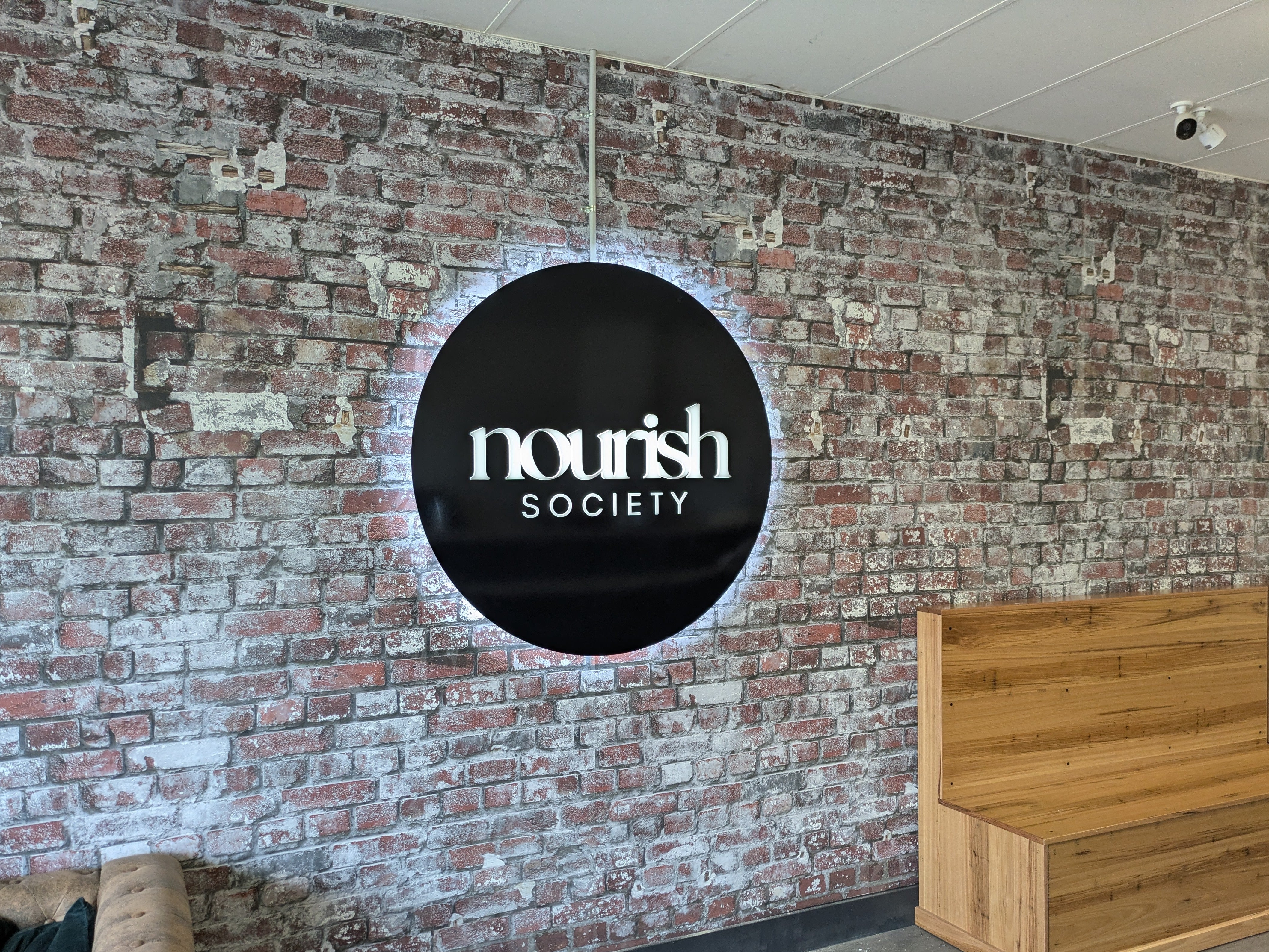 Illuminated round wall sign on brick wall by Saltwater Sign Co